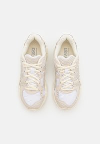 Paire de chaussures de course ASICS beige et blanches avec panneaux en mesh et lacets, vues de dessus sur fond blanc.