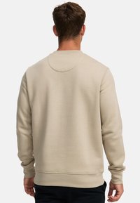 Beige Sweatshirt mit langen Ärmeln, rundem Ausschnitt und gerippten Bündchen. Glatte Textur, minimalistische Details und flache Nähte auf der Rückseite.