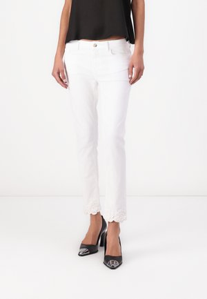 White jeans with a slim fit, featuring a delicate lace trim at the hem. Paired with black pointy-toed heels with a metallic accent.