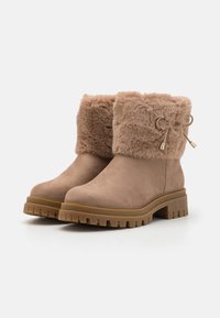 Brune suede ankelstøvler med faux pelskant, rund tå og chunky gummisåle med et teksturert mønster. Bronse detaljer.