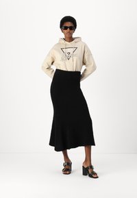 Krémová mikina s grafickým potiskem, černá strukturovaná midi sukně a černé sandály na blokovém podpatku se zlatými akcenty. Moderní neformální outfit.