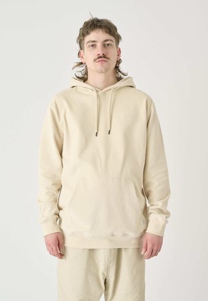 Beige hoodie with a front pocket, drawstring hood, and subtle logo detail. Made of soft, textured fabric with ribbed cuffs and hem.