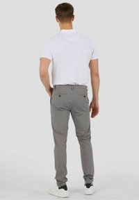 Pantalones grises de material ligero, con un ajuste slim, dos bolsillos traseros con botones y un dobladillo limpio. Se llevan con una camiseta polo blanca.