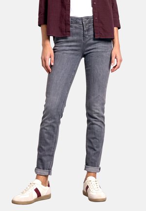 Femme portant un jean skinny gris retroussé et des baskets blanches avec des rayures rouges, assortis à une chemise bordeaux boutonnée et un haut blanc.