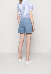 Ljust blå bomullsshorts med en bakficka och en liten knappdetalj, ihop med en blå och vit randig kortärmad skjorta.