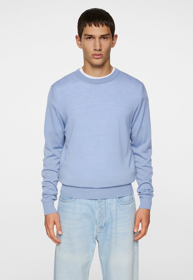 Light blue knit sweater with a crew neckline and long sleeves, featuring a ribbed hem and cuffs, paired with light denim jeans.