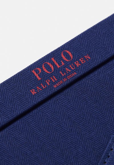 Tamsiai mėlynos spalvos audinys su deimantiniu raštu, su raudonu tekstu "POLO RALPH LAUREN" ir detale "MADE IN INDIA".