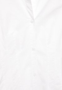 Chemise blanche boutonnée devant montrant trois boutons et un col en V, tissu uni avec de légères rides.
