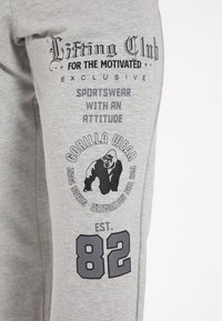 Grijze sweats met een zachte textuur, voorzien van zwarte bedrukte graphics, waaronder een gorilla-logo, tekst en het nummer "82."