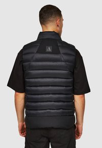 Sort puffer-vest med vandrette syninger, en høj krave og logo-patch ved halsen. Glat stof med en let tekstur.