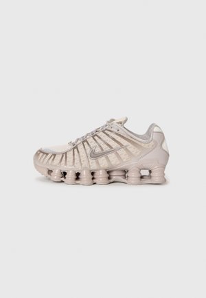 Baskets Nike beige avec empeigne translucide, bandes verticales distinctes et semelle segmentée amortie conçues pour un usage sportif.