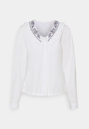 Blouse blanche à manches longues avec col à volants orné de broderies florales et fermeture à boutons sur le devant.