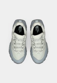 Ζευγάρι λευκά και γκρι παπούτσια πεζοπορίας North Face με κορδόνια, σε θέα από πάνω πάνω σε απλό ανοιχτόχρωμο φόντο.