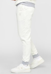 Vita sweatpants med smal passform, utrustade med grå mudd, sidofickor och en diskret logotypdetalj på låret. Bärs med vita sneakers.