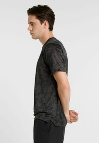 Black short-sleeve t-shirt with a subtle textured pattern and crew neckline, displayed from the side, paired with black shorts.