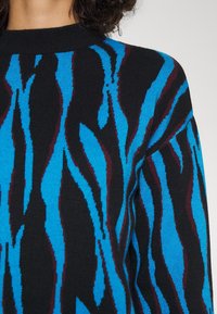 Pull noir avec des motifs ondulés bleus et bourgognes. Présente un col rond classique et un tissu tricoté texturé. Vue en gros plan de la partie supérieure.