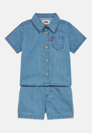 Lys blå denimskjorte med korte ermer, knapper og brystlomme, kombinert med matchende denimshorts.