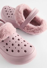 Roze klompen met een fuzzy roze bontvoering, voorzien van ventilatiegaten en een achterriem voor een veilige pasvorm. Gemaakt van glad, duurzaam materiaal.