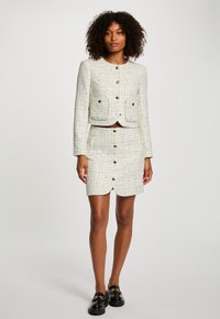 Abito due pezzi bianco in tweed composto da una giacca corta con due tasche a bottone e una gonna al ginocchio con bottoni frontali.