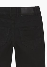 Zwarte spijkerbroek van denim met een gladde textuur, een leren label op de taille en twee schuin aangebrachte achterzakken met nette stiksels.