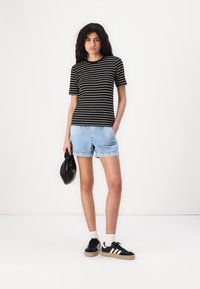 Black and white striped short-sleeve t-shirt paired with light blue denim shorts. Model holds a black handbag and wears black sneakers.