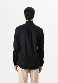 Μαύρο πουκάμισο με μακριά μανίκια φτιαγμένο από λεία ύφανση, με ευθεία σχεδίαση στην πλάτη, διακριτές ραφές στους ώμους και κλασικές κουμπωτές μανσέτες.