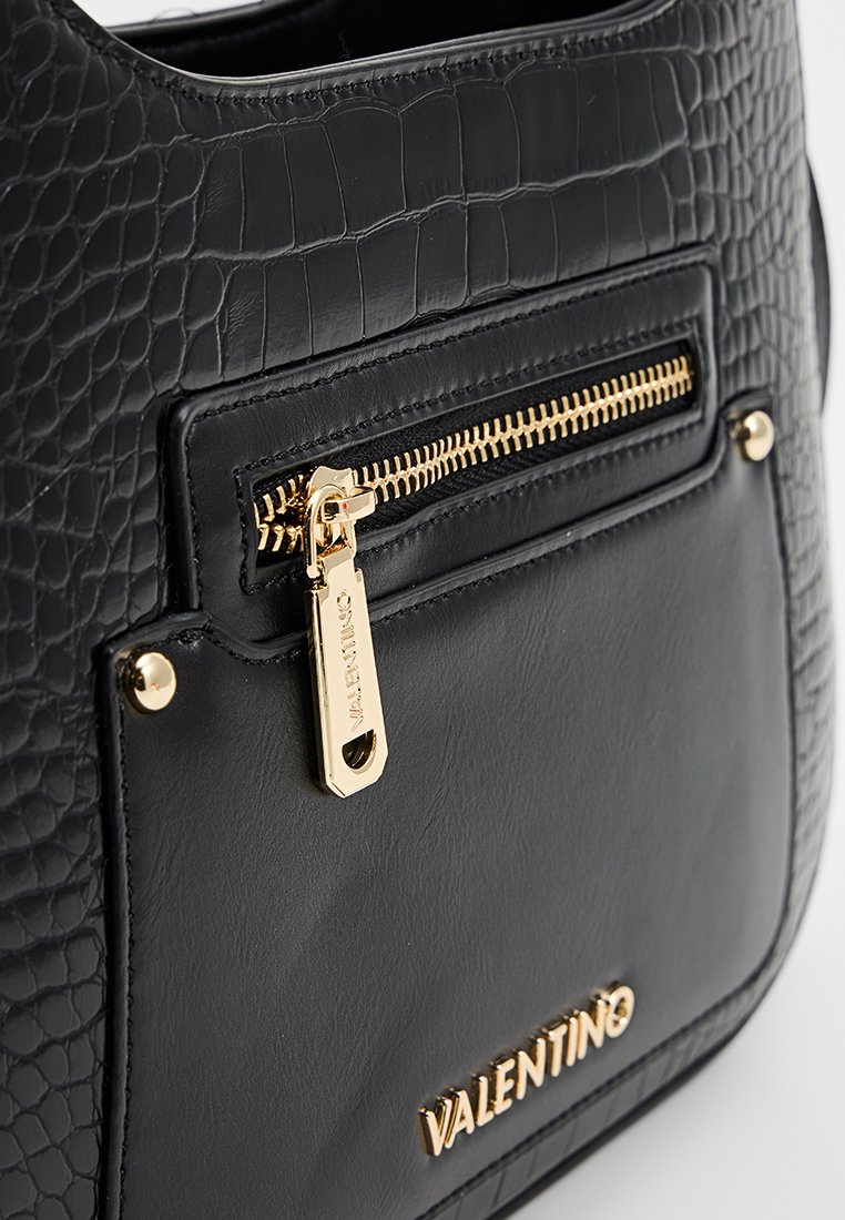 Sac à main noir avec un motif crocodile texturé, doté d'une poche zippée à l'avant avec des accessoires en or et un détail en relief du logo.