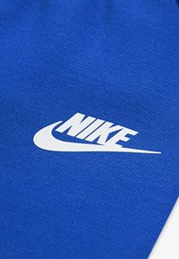 Material textil albastru cu un logo Nike alb proeminent, cu un finisaj neted și linii clare pe un fundal texturat.