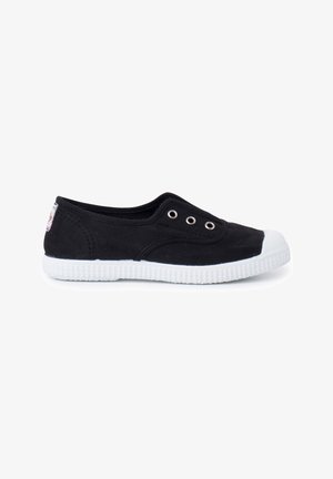 Black low-cut canvas slip-on shoe with white rubber sole and toe cap, featuring three metal eyelets and minimal stitching details.