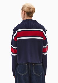 Granatowy krótki sweter z czerwonymi i białymi paskami, prążkowanym kołnierzykiem i fakturowanym splotem. Połączony z ciemnoniebieskimi dżinsami o prostym kroju.