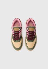 Zapatillas con parte superior de cuero color marrón claro, acentos de ante verde, forro de tela rosa y cordones burdeos. Presenta una suela de goma texturizada.