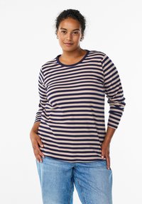 T-shirt rayé à manches longues en beige et marine, avec une texture côtelée, un col rond et une coupe décontractée, assorti à un jean bleu clair.