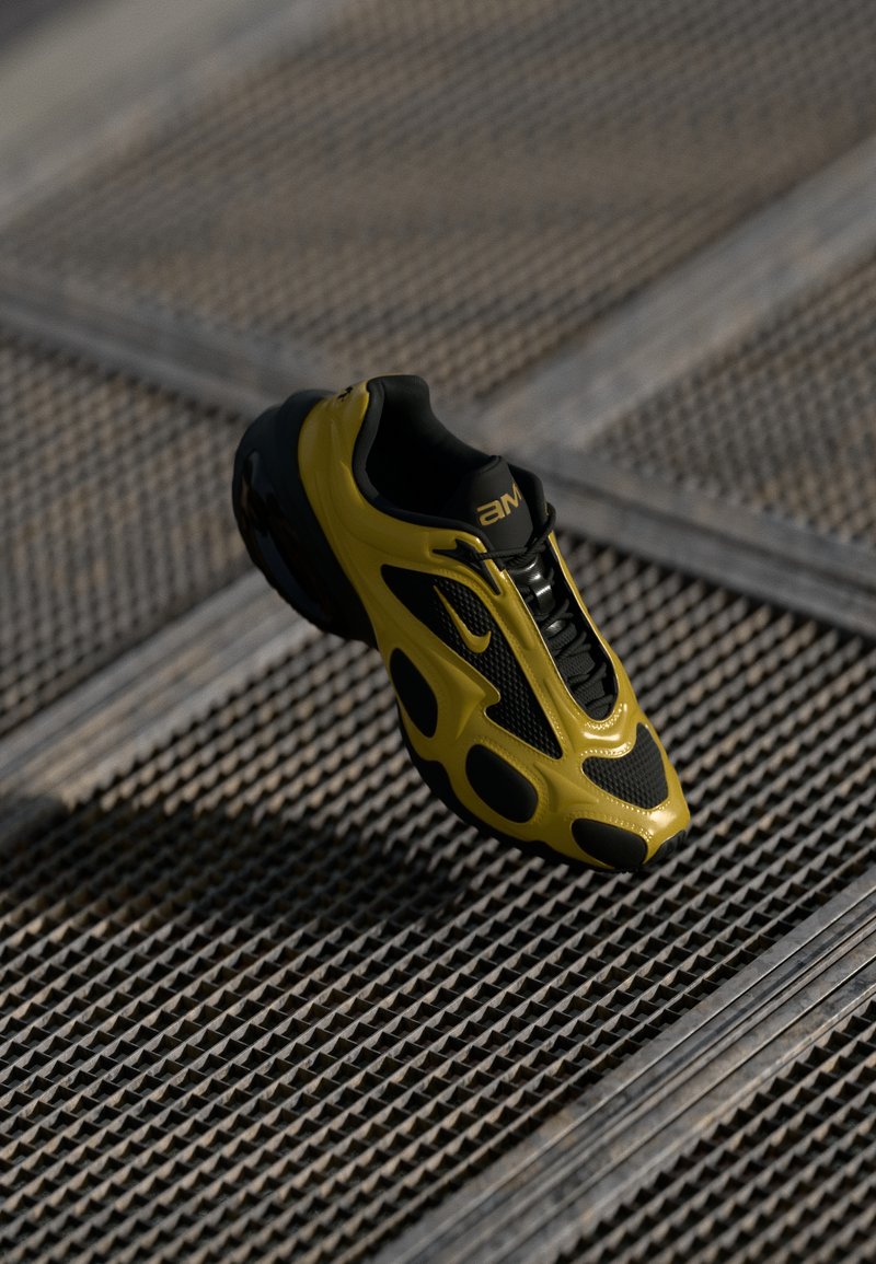 Τα αθλητικά παπούτσια Nike διαθέτουν μαύρο πλέγμα στην επάνω επιφάνεια με κίτρινες λεπτομέρειες, υφή σχεδίασης και μια διακριτική σόλα με κοψίματα, αιωρούμενα πάνω από μεταλλική επιφάνεια.