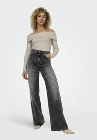 Off-the-shoulder, smulkiai banguota bežinė palaidinė, derinama su juodais aukšto liemens džinsais, turinčiais plačias kojines ir švelnų perėjimą, papildyta smailiais bežiniais aukštakulniais.