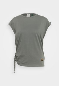 Camiseta casual de manga corta gris con escote redondo, detalle de nudo en el lateral y pequeña etiqueta de marca negra y amarilla cerca del dobladillo sobre fondo liso.