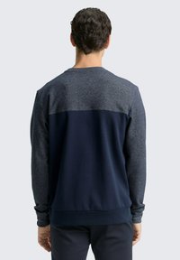 Męska bluza z szarym górnym odcinkiem i granatowym dolnym odcinkiem. Wykonana z cienkiej tkaniny, z długimi rękawami i okrągłym dekoltem.