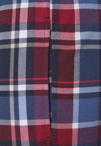 Geruite stof in de kleuren rood, marineblauw, wit en blauw. Geweven textuur met verschillende vierkantpatronen en een zichtbare naad aan de zijkant.