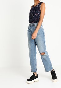 Marinblå ärmlös topp med blommönster, kombinerad med ljusblå slitna jeans och svarta sneakers med tjocka vita sulor.