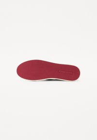 Die Schuhsohle weist eine glatte rote Gummi-Oberfläche mit einem strukturierten Muster auf, umrandet von einem weißen Rand, was auf ein lässiges Sneaker-Design hindeutet.