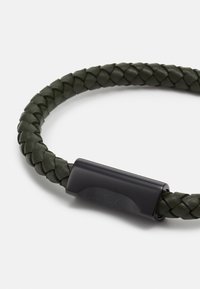 Bracciale in pelle intrecciata verde scuro con una chiusura in metallo nero elegante, dotata di un logo incisa. Design arrotondato, superficie testurizzata.