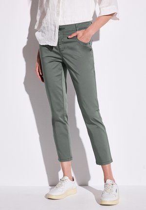 Chinos verde in misto cotone con vestibilità slim, dotati di tasche laterali, orli cuffiati e chiusura con zip, abbinati a sneakers bianche.