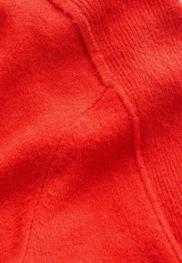 Helles rotes, weiches Gewebe mit sichtbaren Nähten und strukturiertem Strickmuster, das Nahaufnahmen von den Nähten und der Materialoberfläche zeigt.