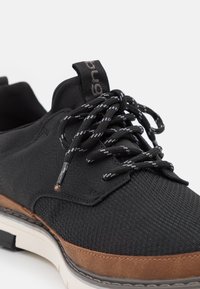 Black sneakers featuring a combination of textured mesh and smooth leather materials, with brown suede accents and contrasting black laces.
