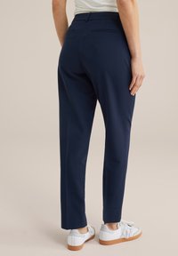Marinblå skräddarsydda byxor med slim fit, mjukt tyg och minimala detaljer. Bärs med vita sneakers som har en strukturerad sula.