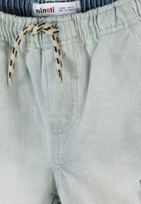 Pantalon bleu clair pour enfants avec une taille élastique, un cordon blanc et noir, et une étiquette indiquant la marque « minoti » et la taille 5-6 ans.