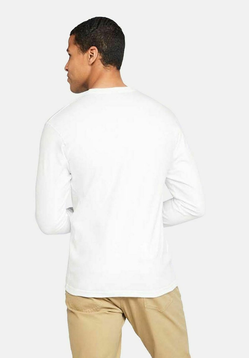 Chemise blanche à manches longues en coton doux, avec un col rond et une coupe décontractée. Associée à un pantalon beige clair, vue de dos.