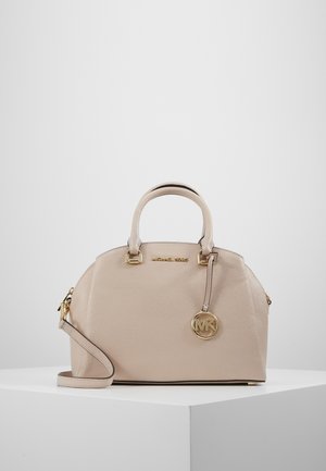 Beige Michael Kors handtas met dubbele handvatten, afneembare schouderriem en gouden MK logo-bedel op een wit voetstuk.