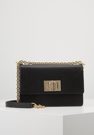 Sac bandoulière en cuir noir avec bandoulière chaîne dorée et fermoir rectangulaire doré orné de détails de logo en relief, présenté sur une surface blanche.