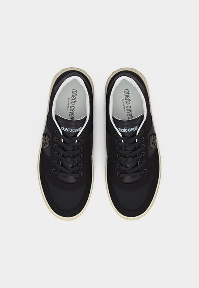 Ζευγάρι μαύρα αθλητικά παπούτσια Roberto Cavalli χαμηλού ύψους με λευκές σόλες, σχέδιο με κορδόνια και λεπτομέρειες λογότυπου στη γλώσσα και τις πλαϊνές πλευρές.