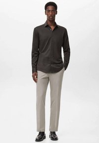 Camisa de botones gris oscuro con cuello estructurado, mangas largas, combinada con pantalones gris claro y zapatos negros para un look minimalista.